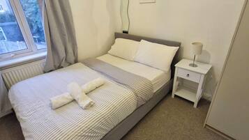 A neatly made bed with a striped bedspread and pillows, a bedside table with a lamp, and a window with curtains.