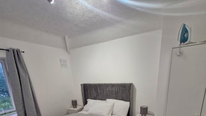 Un dormitorio con cama, mesitas de noche, armario y ventana con cortinas.