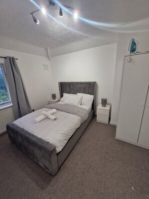 Quarto com cama, mesas de cabeceira, guarda-roupa e janela com cortinas.
