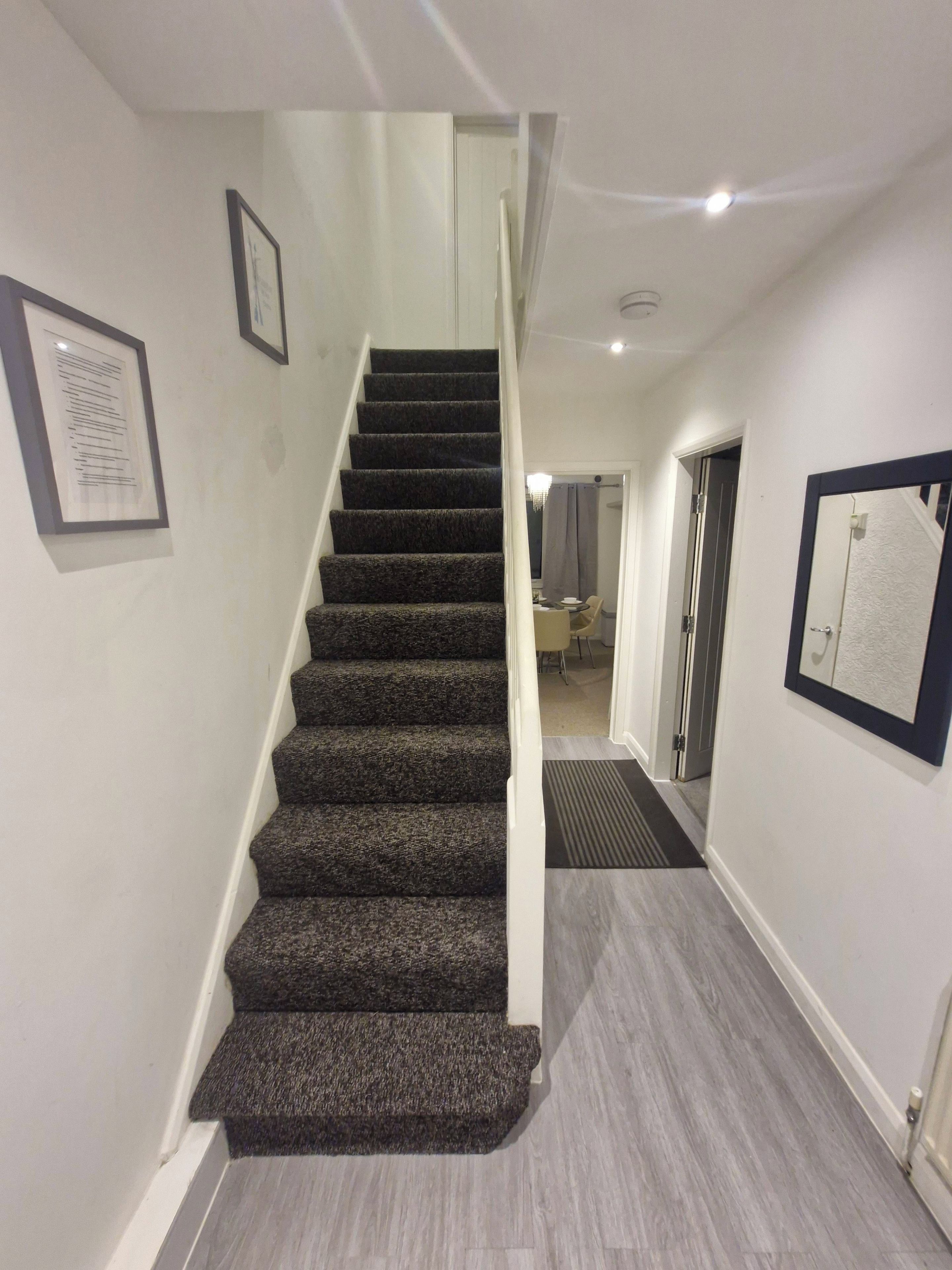 A staircase with carpeted steps leading to a landing, a framed certificate on the wall, and a door leading to another room.
