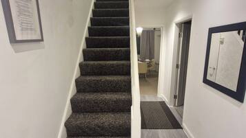 A staircase with carpeted steps leading to a landing, a framed certificate on the wall, and a door leading to another room.