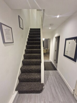 A staircase with carpeted steps leading to a landing, a framed certificate on the wall, and a door leading to another room.