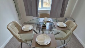Una mesa redonda de vidrio con cuatro sillas, un jarrón con flores, y platos y tazones listos para una comida.