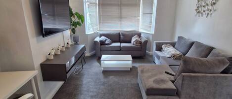 A modern living room with a flat-screen TV, a sofa, a coffee table, and a desk with a chair.