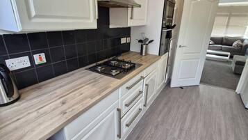 A modern kitchen with white cabinetry, a wooden countertop, and a black tiled backsplash.