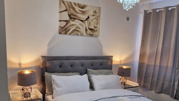 Ein ordentlich bezogenes Bett mit weißen Leinen und zwei aufgerollten Handtüchern, ein mit Wirbeln versehenes Kopfteil, ein an der Wand befestigtes abstraktes Blumenbild und eine Kristallleuchter.