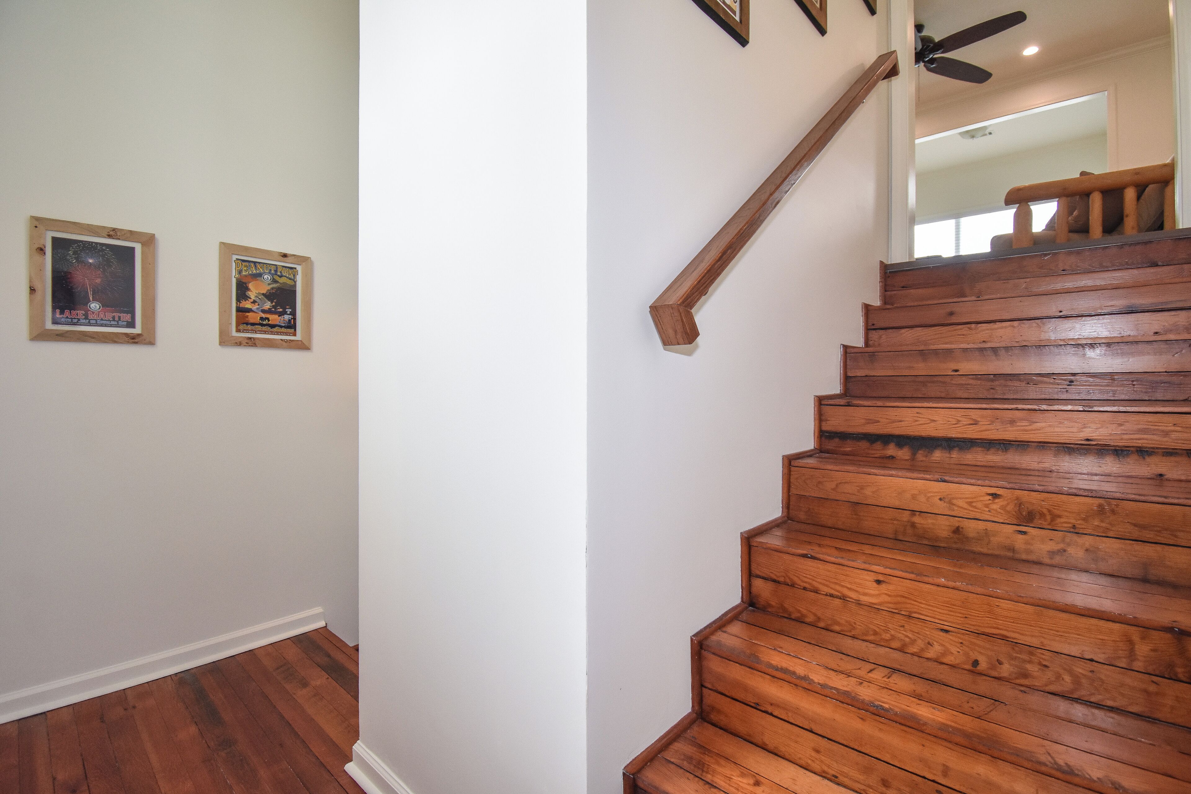 A wooden staircase with a handrail, white walls, and two framed posters on the wall.