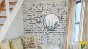 A living room with a white sofa, a patterned rug, a glass coffee table, and a brick-patterned wall. - 183 Orchard St (New York)