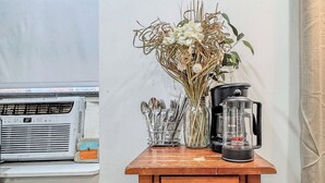A kitchen counter with a coffee maker, utensils, and a vase of dried flowers. There is a wall-mounted sign above the counter. - 183 Orchard St (New York)
