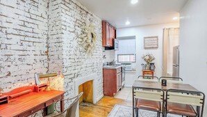 A modern kitchen with white brick walls, wooden flooring, and a dining area with a table and chairs. - 183 Orchard St (New York)