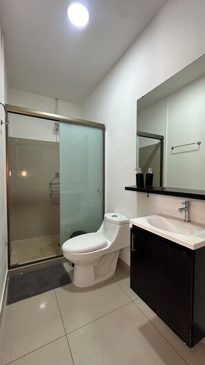 A modern bathroom with a glass shower enclosure, a white toilet, a black vanity with a mirror, and a white sink. - Family House 6 Private Rooms, Antiguo Cuscatlán (Antiguo Cuscatlan, Zona Uca)