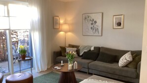 A modern living room with a sofa, a coffee table, and a small side table. There is a window with curtains and a view of the outside. - 4 Star Holiday Home in Vedbaek (Vedbaek)