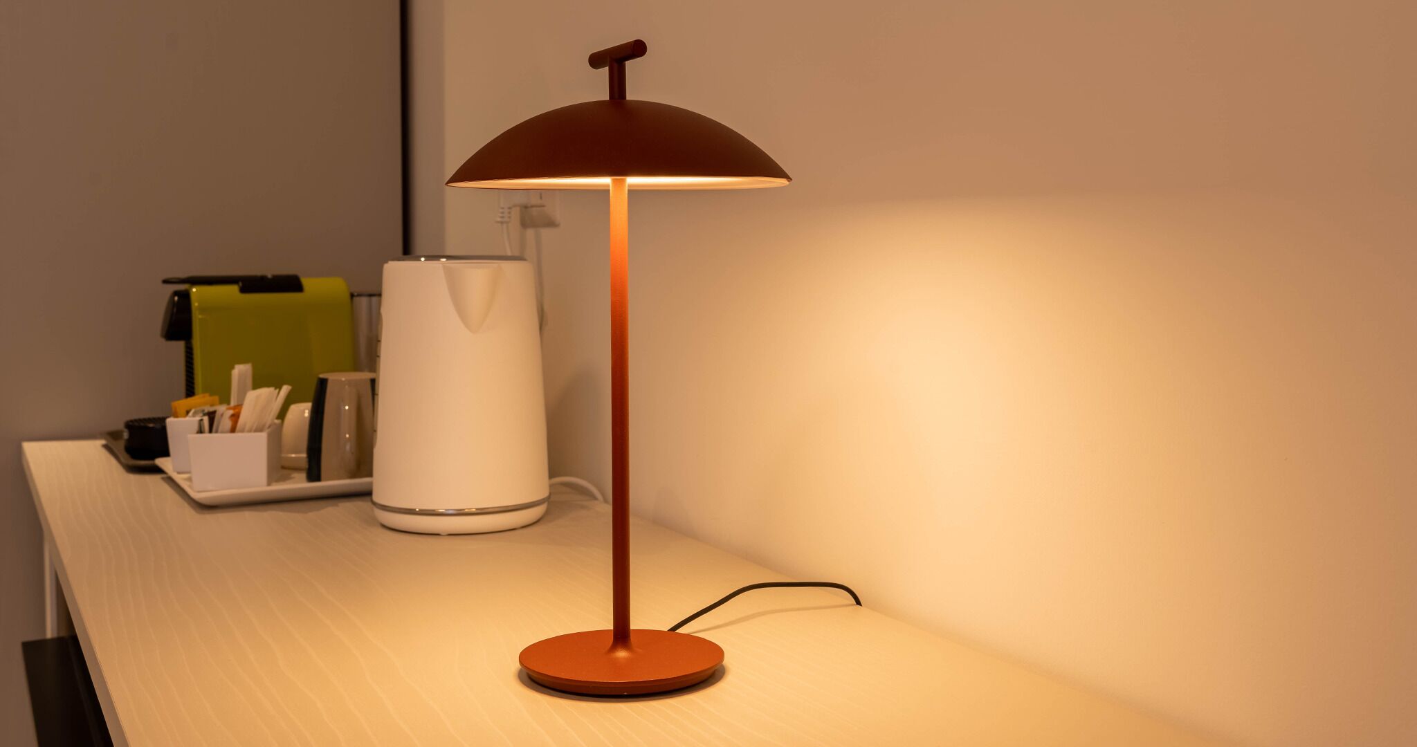 A desk with a lamp, a white cylindrical object, and a tray with stationery.