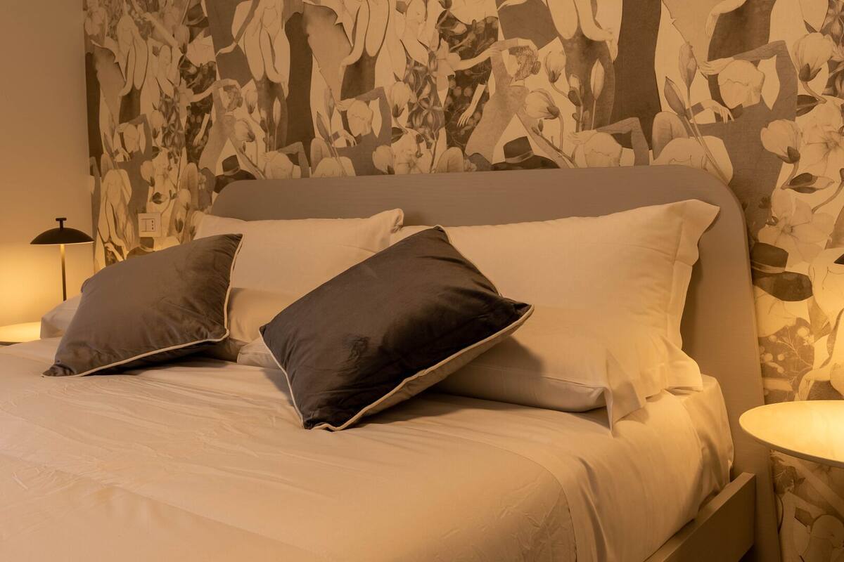 Una cama bien hecha con dos almohadas, un cabecero y dos lámparas de noche.