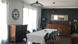 Een eethoek met een lange tafel, stoelen, een houten kast en een donkere muur met een spiegel.