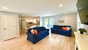 A spacious living area with two blue sofas, a white door, and a kitchen in the background.