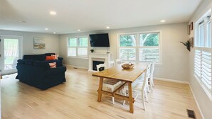 A spacious living room with a dark blue sofa, a wooden dining table, and a fireplace.