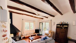 A cozy living room with a sofa, wooden beams, a fireplace, and a television. - Cottage 100m from the beach (CT)