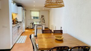 A modern kitchen with white cabinets, a wooden dining table, and a hanging light fixture. - Cottage 100m from the beach (CT)