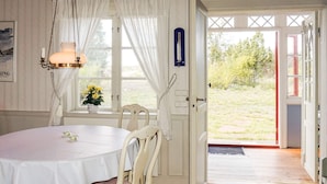 A room with a round table, white chairs, a hanging light fixture, a window with curtains, and a door leading outside. - 6 Person Holiday Home in Oskarshamn (Oskarshamn)