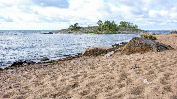 A sandy beach with a rocky outcrop and a small island with trees in the distance. - 6 Person Holiday Home in Oskarshamn (Oskarshamn)