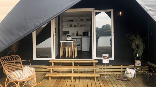 A tent with a wooden deck, a rocking chair, a table, and a kitchen area visible through the entrance. - Lodge Near Antwerp With Nature Trails (Lille)