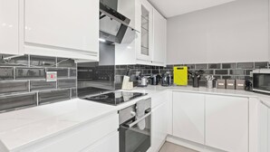 A modern kitchen with white cabinetry, a black tiled backsplash, and stainless steel appliances.