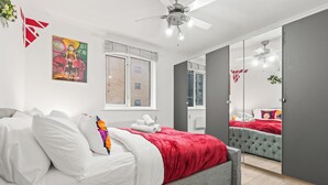A modern bedroom with a grey bed, white bedding, a red throw blanket, and a large mirror.