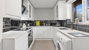 A modern kitchen with white cabinetry, a built-in oven, microwave, and a washing machine.