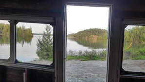 Vista desde una ventana sobre un lago tranquilo con árboles y una colina boscosa a lo lejos.