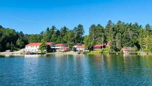 Una propiedad junto al lago con varios edificios de techo rojo, presumiblemente viviendas o casas de vacaciones, ubicada a la orilla del agua y con un denso bosque al fondo.
