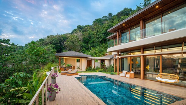 A modern house with a swimming pool, wooden deck, and lush greenery.
