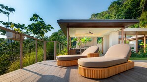 A modern outdoor lounge area with two cushioned seating options, a wooden deck, and a covered seating area with a ceiling fan.