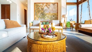 A spacious living room with a large painting, a glass coffee table, and a view of the outdoors.