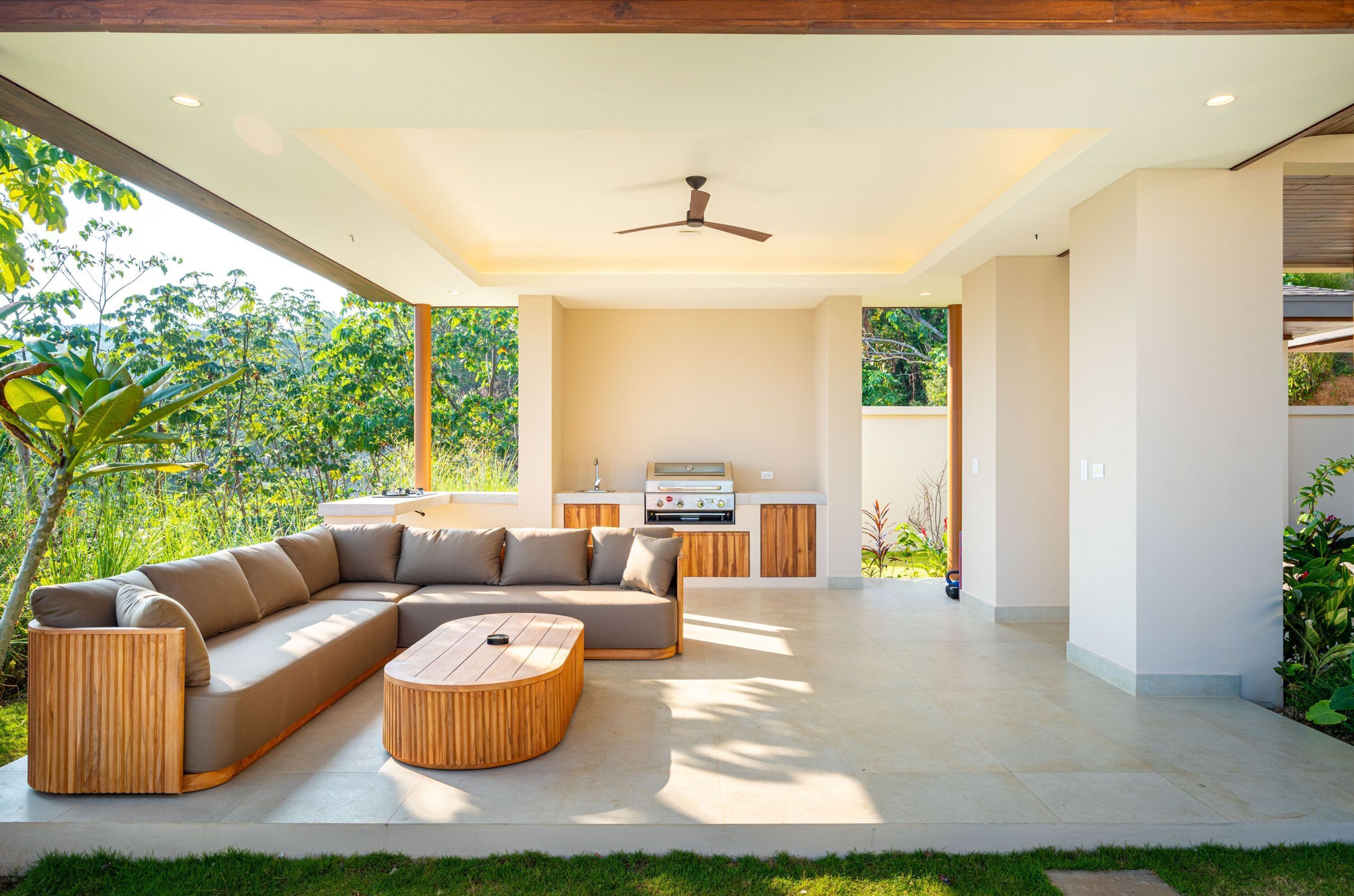 A modern outdoor living area with a sectional sofa, a wooden coffee table, and a built-in grill station.