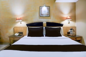 Ett hotellrum med en stor säng, två sänglampor, en inramad tavla på väggen, en telefon vid sängen och ett litet bord med en kaffebryggare.
