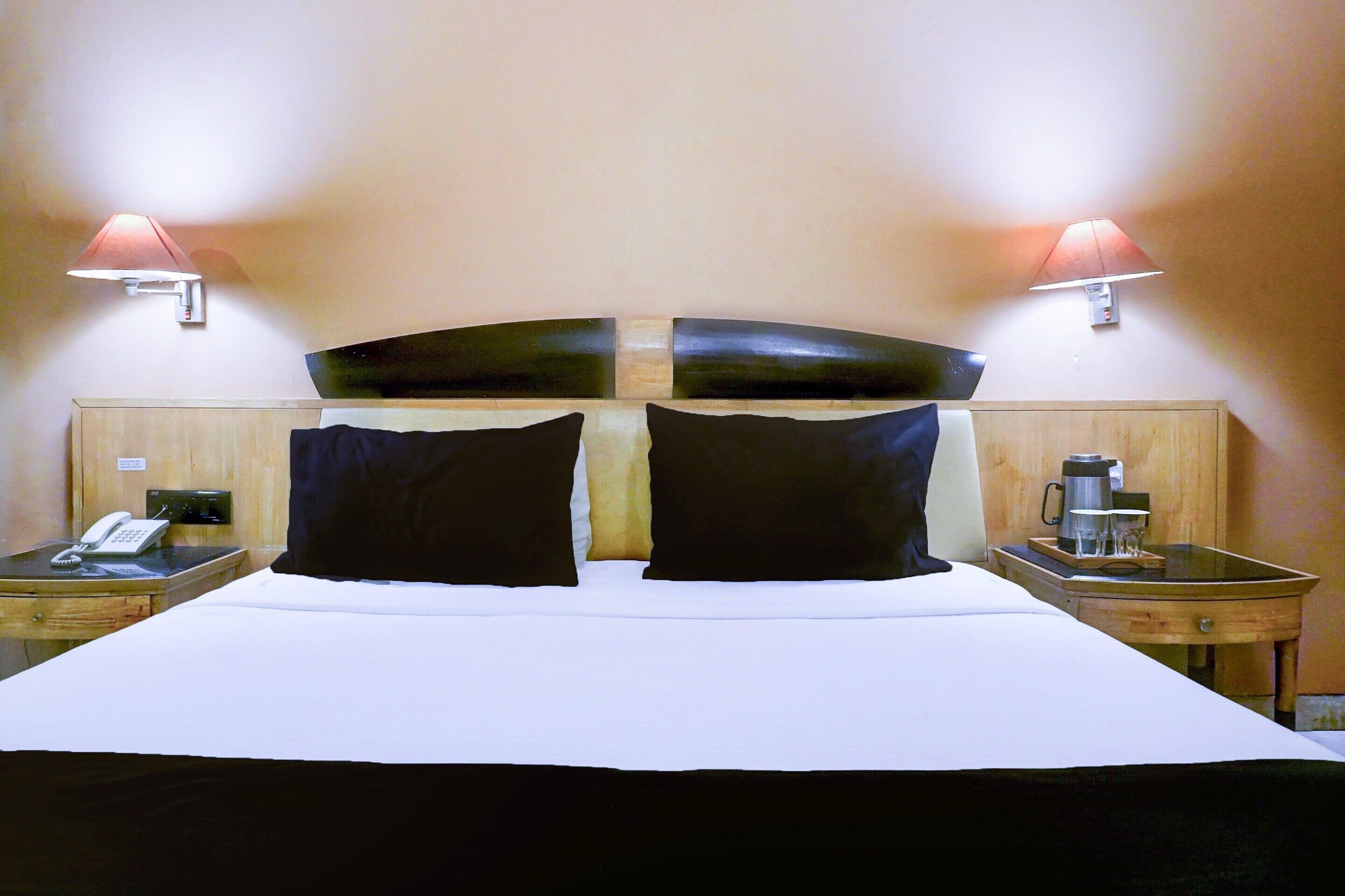 A hotel room with a large bed, two bedside tables, a nightstand, a lamp, and a wall-mounted telephone.