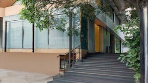 Un escalier extérieur menant à l’entrée d’un bâtiment, entouré de verdure et doté de murs en verre.