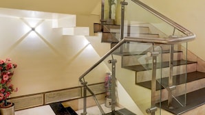Un escalier moderne avec des rampes en verre et des garde-corps en métal, menant à l’étage supérieur.