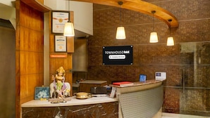 Un espace d’accueil doté d’un comptoir en marbre, de quelques éléments décoratifs en bois et d’un mur en briques. On y trouve des suspensions lumineuses, une enseigne indiquant « Townhouse Oak » et une statue posée sur le comptoir.