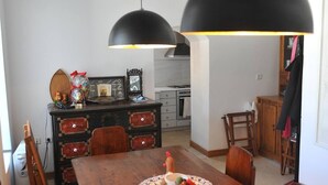 Uma área de jantar com uma mesa de madeira, cadeiras e um prato com comida. Duas luminárias pendentes pretas estão acima da mesa.