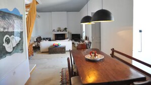 Uma sala de estar ampla com uma mesa de jantar de madeira, um sofá e uma TV ao fundo.