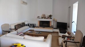 Uma sala de estar com sofá, poltronas, mesa de centro, lareira, televisão e estante de livros.