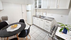 Una cocina compacta con armarios blancos, encimera negra y un pequeño comedor con mesa y sillas.
