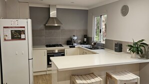 A modern kitchen with a central island, wooden stools, a stainless steel range hood, and a refrigerator with emergency information.
