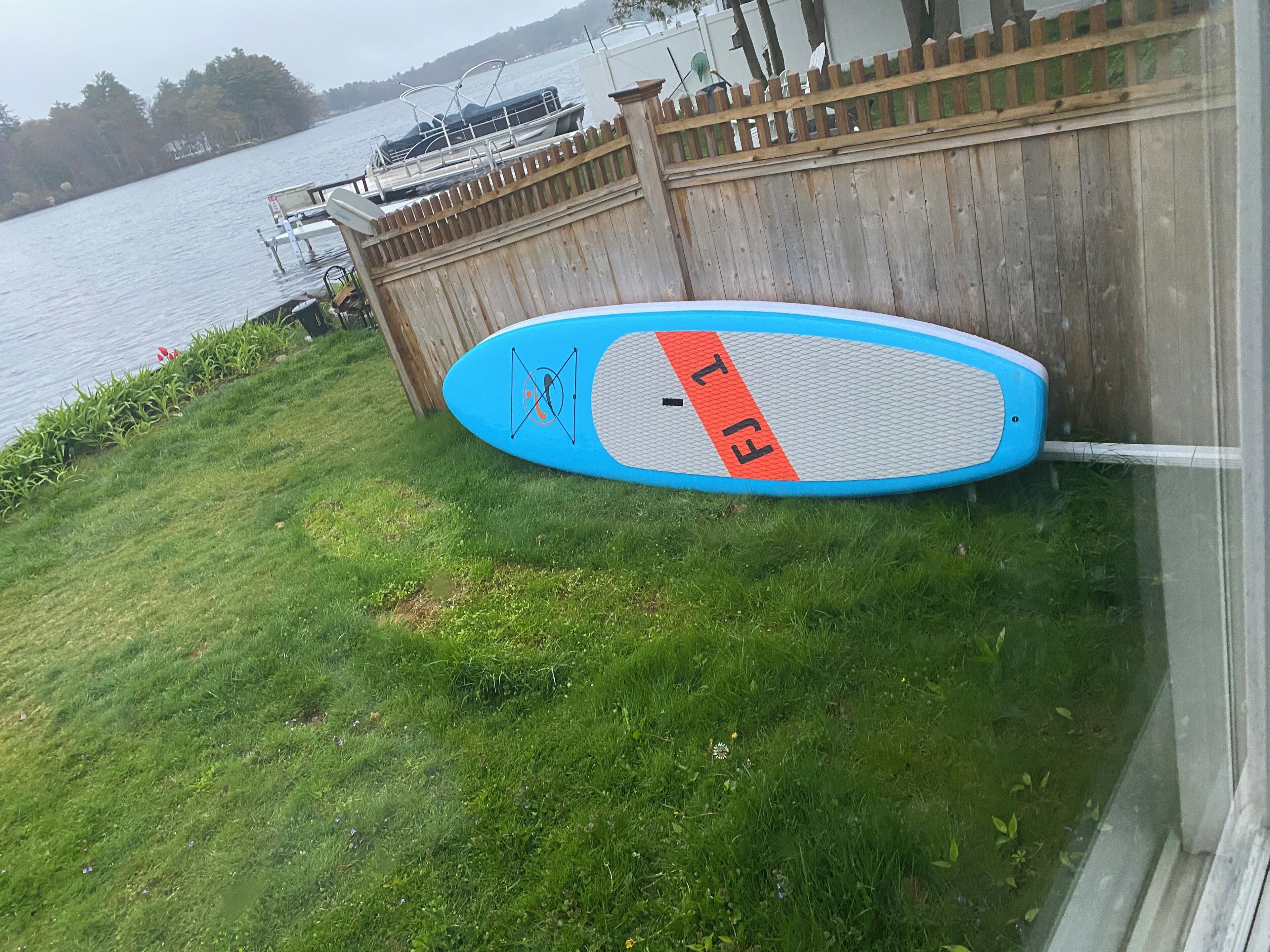 Ein blaues Paddleboard mit dem Schriftzug "EAT", das an einem Holzzaun in der Nähe von Wasser lehnt.
