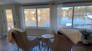Ein Zimmer mit zwei Korbstühlen, einem kleinen runden Tisch und Seeblick durch große Fenster.