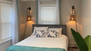 Ein Schlafzimmer mit einem Bett, zwei Nachttischlampen, einem Fenster mit Vorhängen und einer Pflanze.