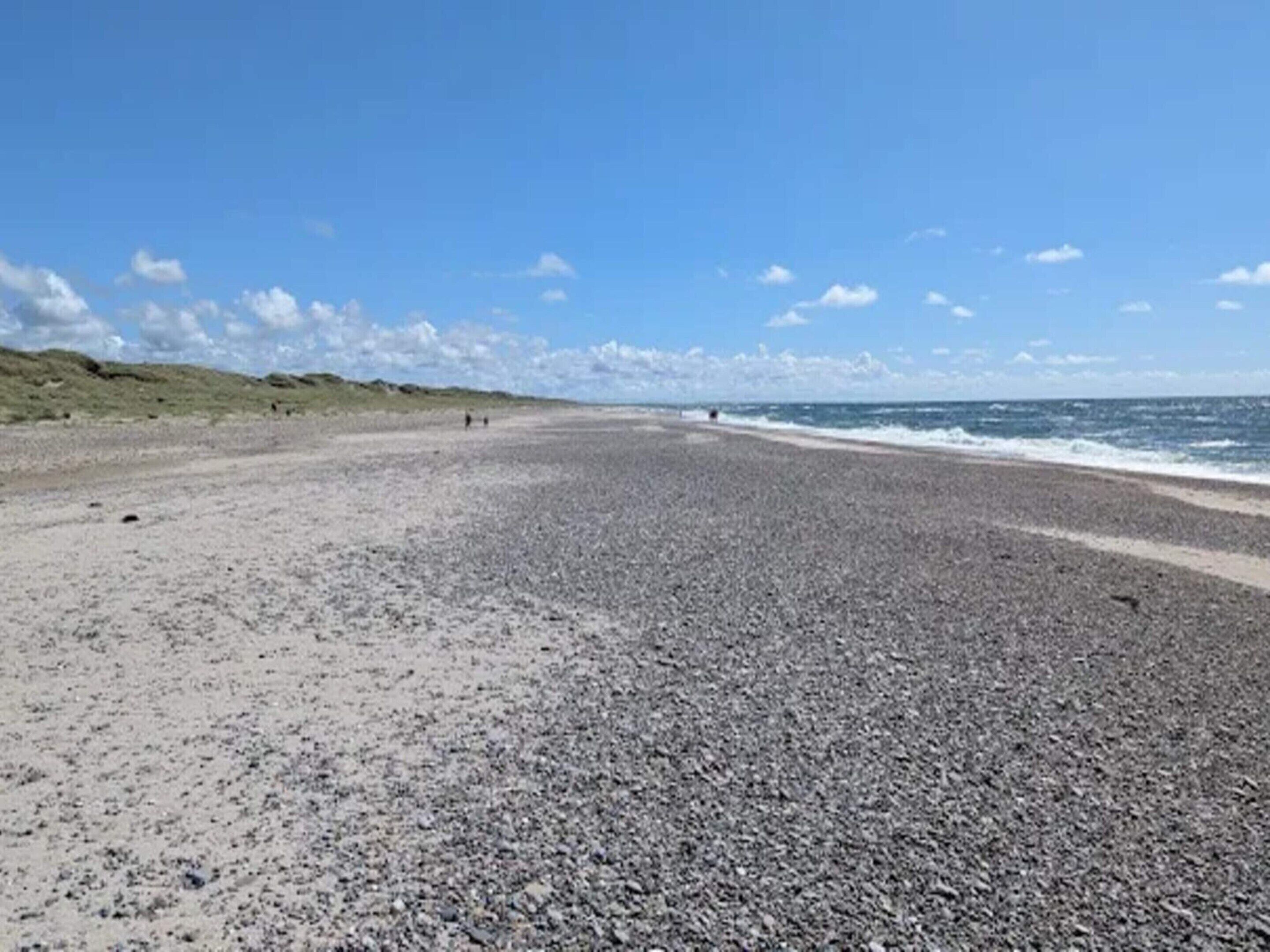 A pebbled beach with a clear sky and distant dunes.