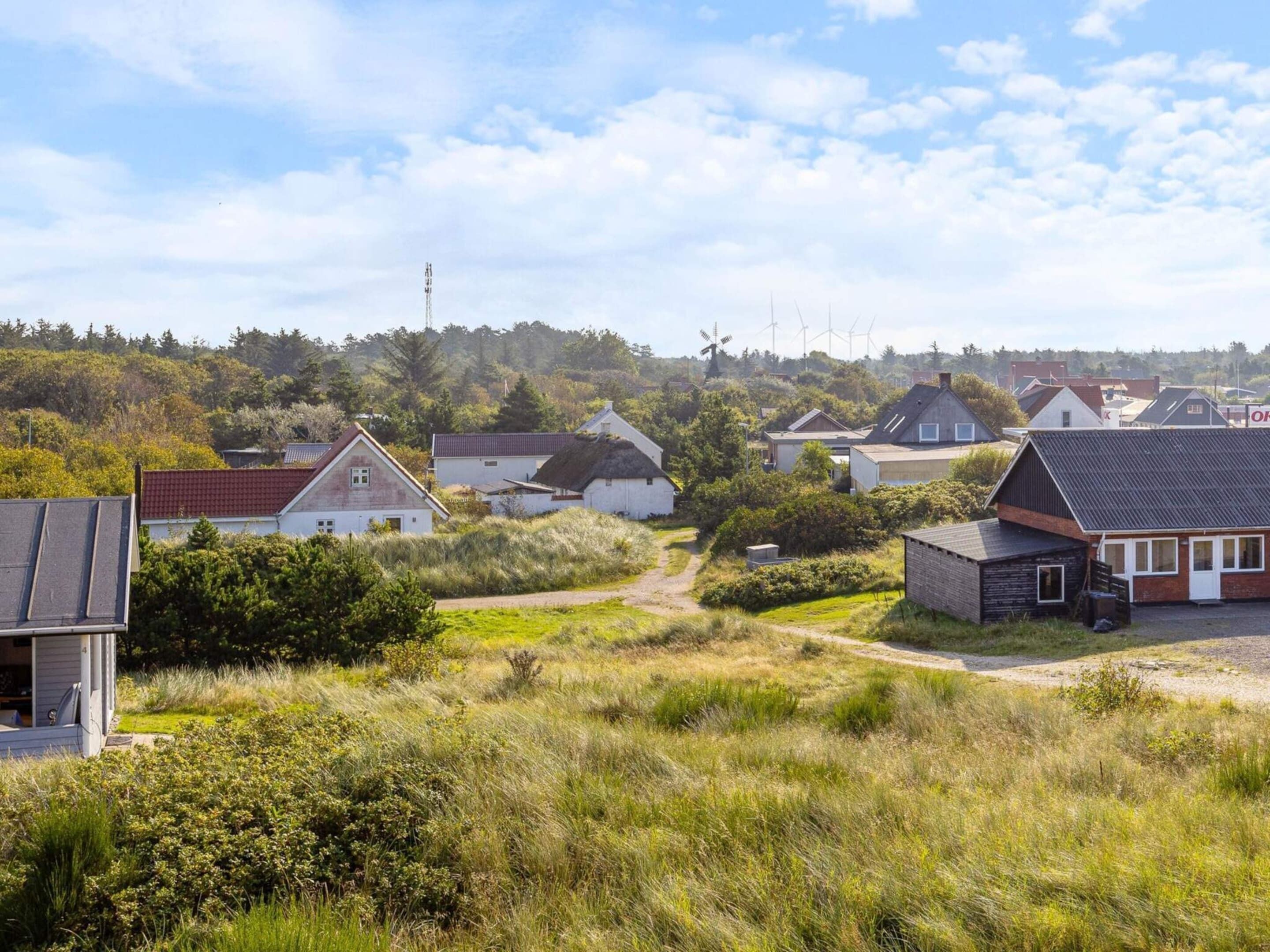 En landlig landsby med traditionelle huse, en støvet sti og vindmøller i baggrunden.